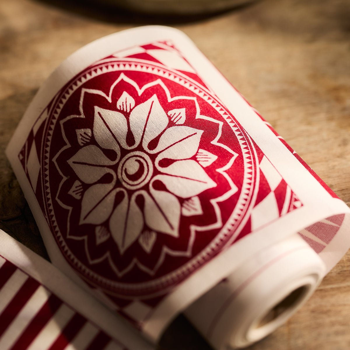 The MY DRAP Holiday Fun Cocktail Napkin Rolls, set of 2, are partially unrolled on a wooden surface, showcasing delightful red and white concentric floral designs perfect for crafting elegant napkins.